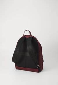 Batoh s marónovým telom a čiernymi sieťovými popruhmi. Zaoblený tvar, vybavený horným úchytom a elegantným dizajnom pre ľahké prenášanie.