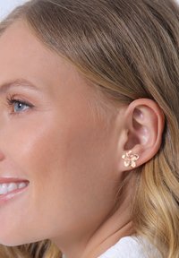 Ohrringe in Form einer Blume aus roségold mit strukturierten Blütenblättern, präsentiert am Ohr eines hellhäutigen Modells, das das Design und Material betont.
