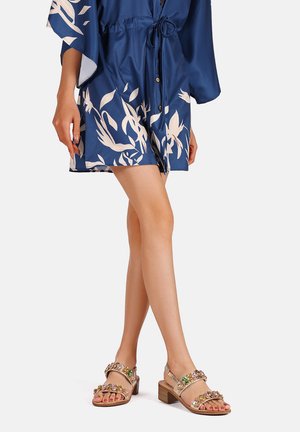Abito stile kimono in navy con motivo floreale, vita cin cinata e bottoni, abbinato a sandali beige con decorazioni di strass e tacco largo.