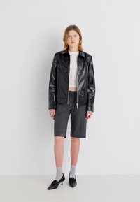 Sort læderjakke med lynlås, hvid cropped top, grå stribede shorts, grå sokker, sorte spidse sko. Glatte teksturer hele vejen igennem.