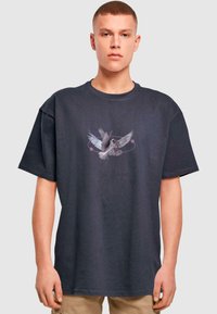 Mørkegrå bomulds-t-shirt med et grafisk motiv af en fugl i flugt, med lyserøde accenter og et cirkulært designelement. Afslappet pasform.