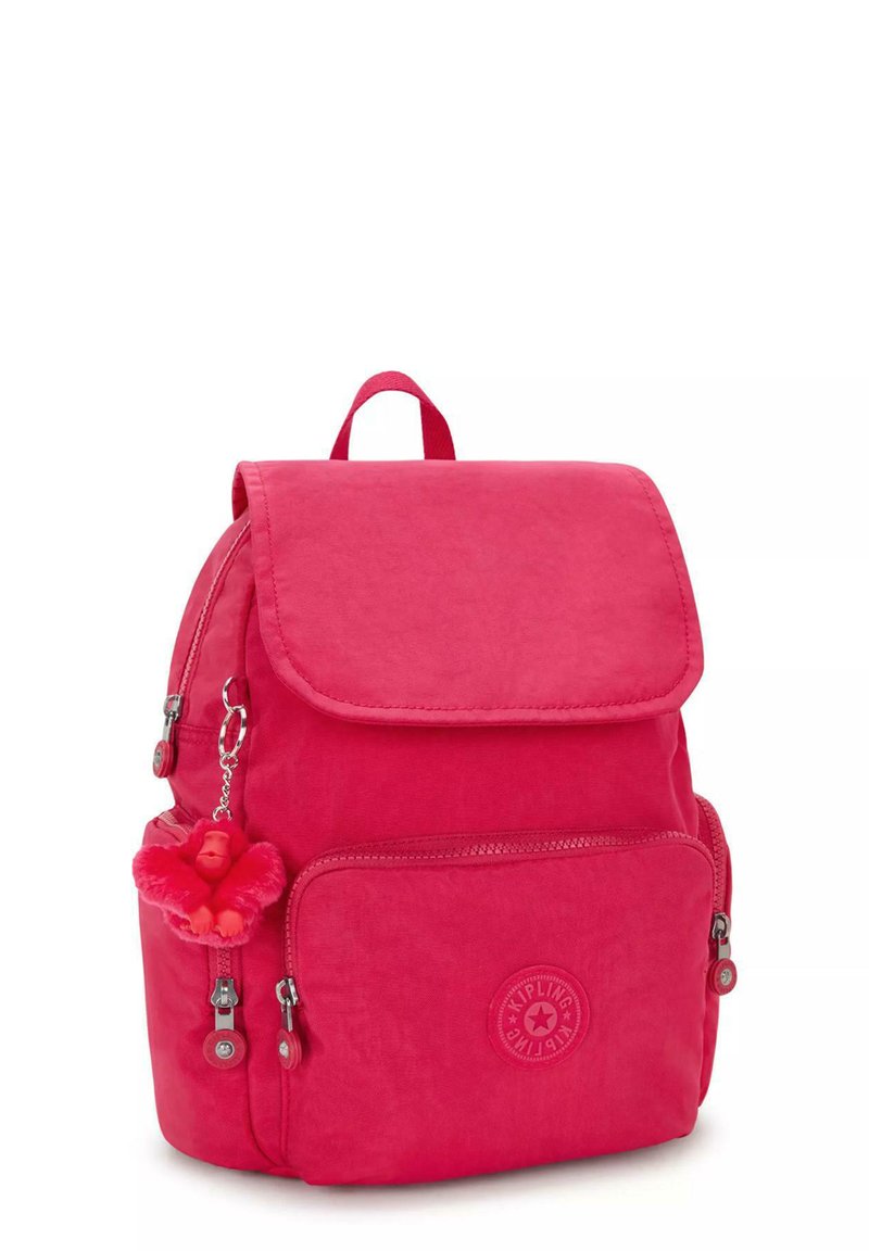 Un sac à dos en nylon rose avec une fermeture à rabat, une poche zippée à l'avant, un logo et un porte-clés comprenant un petit accessoire en peluche de singe rouge.