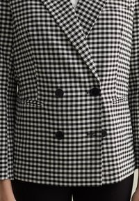 Blazer a rayas en blanco y negro de doble botonadura con un cuello afilado, que presenta botones negros y un ajuste entallado. Detalle de tejido texturizado.