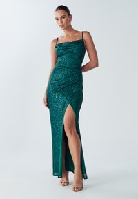 Grøn palietkjole med figursyet silhuet, spaghetti-stropper og slids højt oppe på låret. Glat tekstur med en detalje med rynket halsudskæring.