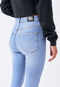 Skinny denim jeans in lichtblauw, met een hoge taille, achterzakken en contrasterende stiksels. Zwarte label zichtbaar bij de taille.