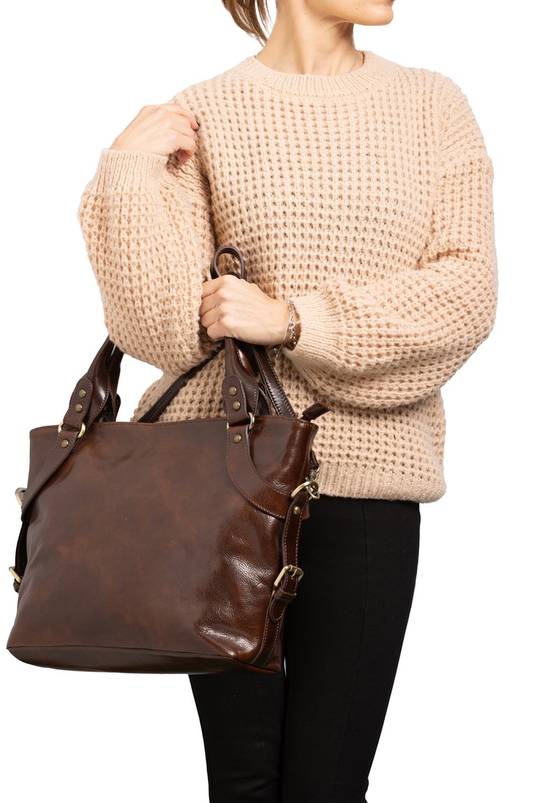Borsa tote in pelle marrone con grande corpo, doppie maniglie e dettagli in metallo dorato. Indossata con un maglione beige testurizzato e pantaloni neri.