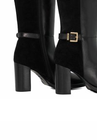 Black knee-high boots in leather and suede, featuring a side zipper, a front strap with a gold buckle, and a chunky black heel.