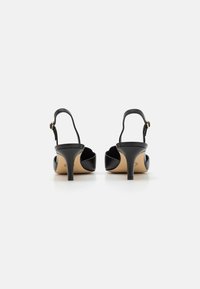 Bottines noires en cuir avec une finition brillante, bout pointu et talon fin. Présente un accent de boucle en ton doré.