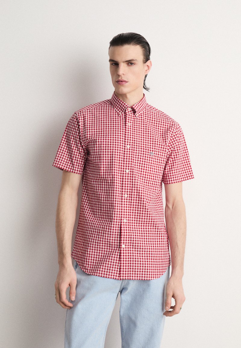 Chemise à manches courtes à carreaux rouges et blancs avec un col boutonné, ornée d'un petit logo sur la poche poitrine, fabriquée en tissu léger.