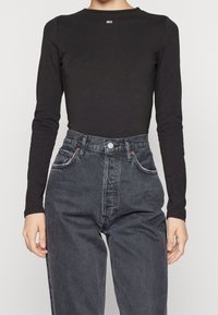 Top nero a maniche lunghe abbinato a jeans grigio scuro a vita alta. Il top presenta un collo rotondo e una piccola etichetta con logo.