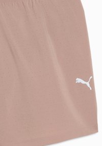 Ελαφρώς ροζ ύφασμα με μικρές διάτρητες τρύπες και μικρό λευκό λογότυπο Puma κοντά στο κάτω άκρο.