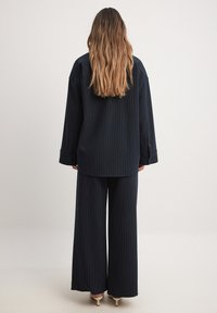 Jūras spēku izstrādāts uzsvērts krekls ar garām piedurknēm, kas apvienots ar atbilstošām platām biksēm, no abiem izgatavots no strukturēta auduma un brīvā piegriezumā.