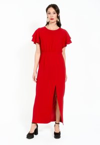 Rochie lungă roșie, cu mâneci învolburate, talie strânsă și o fante pe lateral. Purtată cu pantofi cu toc înalt negri. Culoare solidă, textură netedă.