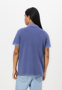 Short-sleeve polo shirt in dark blue cotton with a collar. Features a side slit at the hem and visible stitching details.