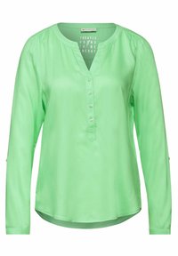 Långärmad blus i ljusgrön färg med en slät tygkvalitet, V-ringning, fem knäppningar och subtila rynkor vid axlarna.