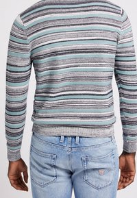 Gestreifter Pullover in Grau, Türkis und Schwarz, mit einem gerippten Saum und Bündchen, kombiniert mit hellblauen Jeans mit Gesäßtaschen und Branding.
