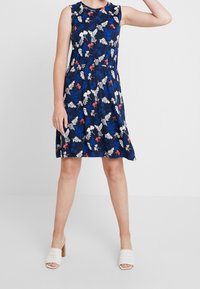 Robe florale bleu marine à la coupe décontractée, sans manches, avec une taille froncée. Elle présente des motifs floraux multicolores et une texture douce.