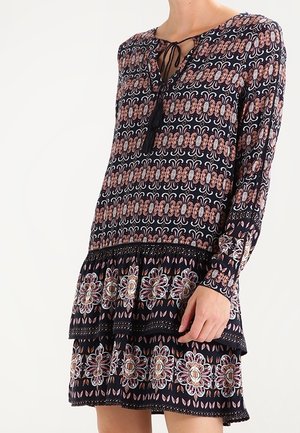 Robe noire à manches longues avec des motifs floraux et géométriques complexes en rose et blanc, dotée d'un détail à nouer au col et d'une jupe à volants.