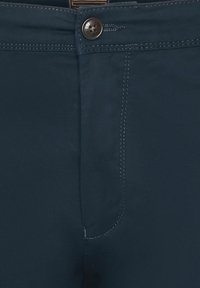 Pantalons bleu marine avec une texture lisse, dotés d'une fermeture éclair centrale, d'un bouton et de coutures contrastées le long des coutures.