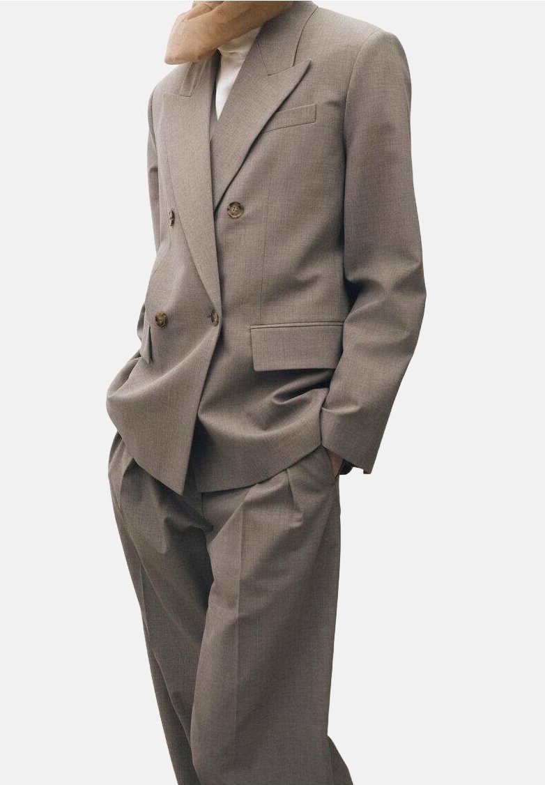 Personne portant un costume taupe ample à double boutonnage avec un pantalon large assorti et un col roulé blanc en dessous.