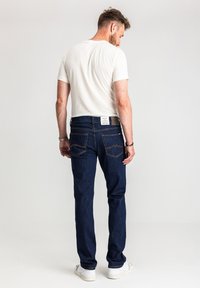 Ciemnoniebieskie jeansy z denimu o prostym kroju, z kontrastowymi przeszyciami, dwoma tylnymi kieszeniami oraz białą metką na pasku.