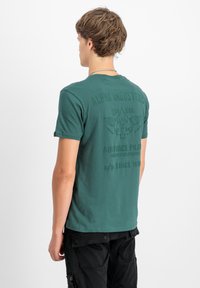 Zelené bavlněné tričko s kulatým výstřihem, na zadní straně s embosovaným textem a grafikou. Krátké rukávy, volný střih.