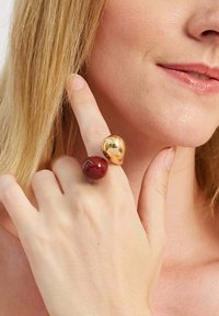 Złote i czerwone pierścionki na palcach, z błyszczącym wykończeniem, okrągłymi kształtami i gładką fakturą, noszone na częściowo widocznej dłoni.