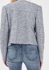 Blazer texturé à manches longues à rayures bleu marine et blanches, avec un ourlet raccourci et des épaules structurées, assorti à un jean bleu clair.