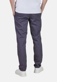 Dunkelgraue Chinos aus Baumwolle. Mit geradem Bein und subtiler Struktur. Kombiniert mit einem weißen T-Shirt und weißen Sneakers.