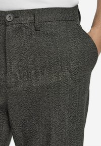 Pantalons en chevron gris avec une finition texturée, dotés d'une poche frontale et d'une fermeture à bouton, fabriqués à partir d'un tissu tissé.