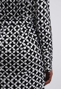 Robe à motifs noir et blanc avec des formes circulaires abstraites, manches longues et ceinture ajustée à la taille.