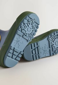 Siniset kumikengät, joissa on vihreä teksturoitu pohja, jossa on leikkisä roiskemalli ja tartuntakuvio pidon parantamiseksi.