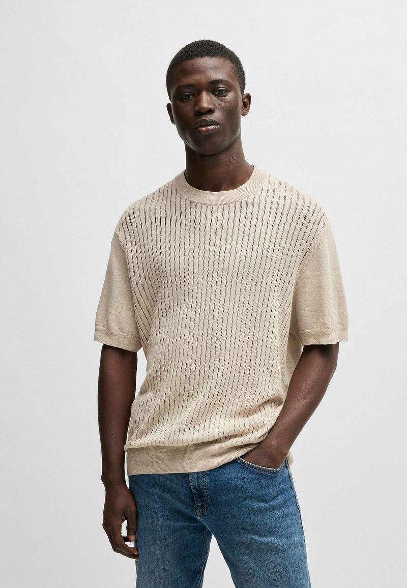 Beige lightweight knit sweater with horizontal ribbing pattern, short sleeves, and crew neckline, worn with blue denim jeans.