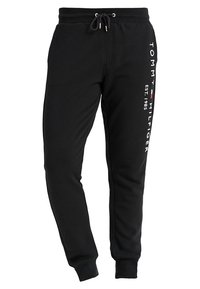 Czarne spodnie dresowe z elastycznym pasem i sznurkiem. Na nogawce znajduje się biały nadruk i logo. Miękki materiał, zwężane u dołu nogawki.