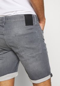 Grå denimshorts med rullad fåll, med en svart märkeslapp på den bakre midjan och två bakfickor. Slät textur och figursydd design.