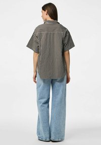 Camicia a righe bianco e nero a maniche corte, vestibilità rilassata, vista posteriore, abbinata a jeans a gamba larga blu chiaro. Tessuto dalla superficie liscia.