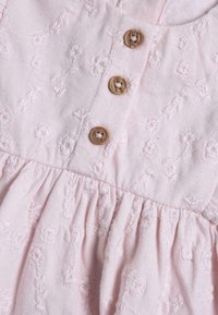 Light pink dress with floral embroidery, featuring three wooden buttons at the bodice and gathered texture at the waist.