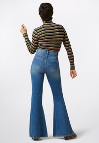 Raidallinen pitkähihaista toppia korkean kaula-aukon kanssa yhdistettynä korkeavyötäröisiin, leveneviin sinisiin farkkuihin. Ominaisuuksiin kuuluu takataskut ja hiukan haalistunut väri.