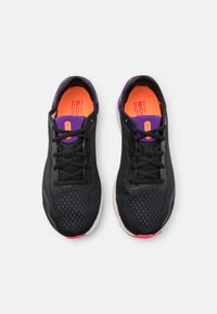 Scarpe sportive nere con tomaia in mesh, dettagli viola e solette arancioni brillanti. Presentano lacci tradizionali e suole bianche ammortizzate.