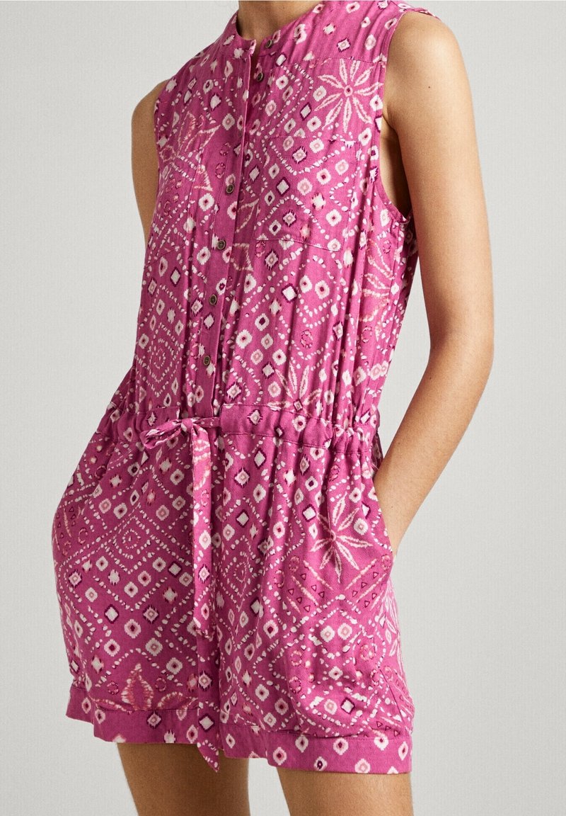 Ärmlös rosa jumpsuit med ett mönstrat mönster, som har knappar, justerbart midjeband och fickor. Tyget verkar mjukt och lätt.
