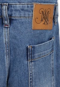 Jeans in denim di colore azzurro chiaro, con un'etichetta in pelle con logo e una tasca frontale. Cuciture visibili e tessuto testurizzato.