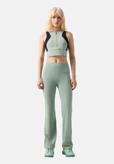 Femme aux cheveux blonds portant un crop top sans manches vert menthe et noir, un pantalon taille haute assorti et des chaussures vert menthe, debout droit.