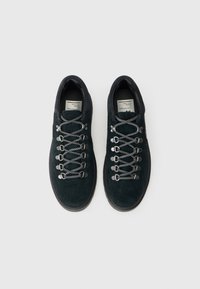 Botas de caminhada em camurça verde-escuro, com biqueira arredondada, ilhós de metal e atacadores com padrão preto e branco. Sola de borracha para tração.