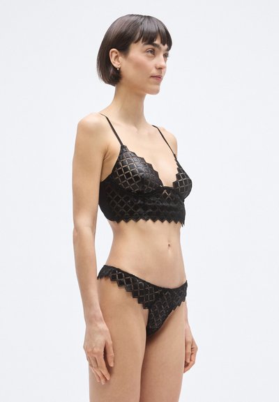 Čierna čipkovaná súprava spodného prádla s diamantovým vzorom, zakončená oblými okrajmi a s nastaviteľnými ramienkami na podprsenke a zodpovedajúcich vysokých nohavičkách.