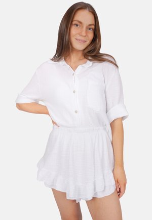 Chemise blanche à manches retroussées, en tissu texturé avec une poche, associée à une jupe évasée à volants.