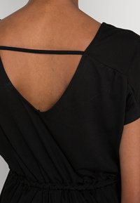 Schwarzes Kleid mit V-Ausschnitt-Design, dünnen Trägern und elastischem Bund. Der Stoff wirkt weich und leicht.