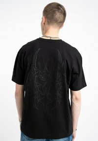 Czarny bawełniany T-shirt z dużym, abstrakcyjnym szarym wzorem na plecach. Krótkie rękawy i luźny krój.