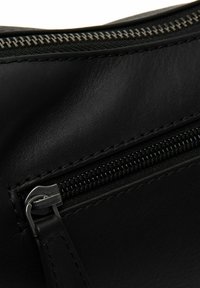 Musta nahkainen laukku, jossa näkyvä vetoketju, esittelee sileän pinnan ja hienot ompeleet. Varustettu metallisella vetoketjun nyökillä turvallista sulkemista varten.