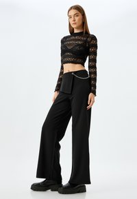 Zwarte kanten crop top met lange mouwen en een gemustreerde textuur, gecombineerd met zwarte wijde broek met een kettingaccent op de taille.