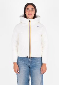 Witte pufferjack met een capuchon, voorzien van een rits aan de voorkant met multikleuren strepen en een trekkoord aan de zoom. Model draagt blauwe spijkerbroek.
